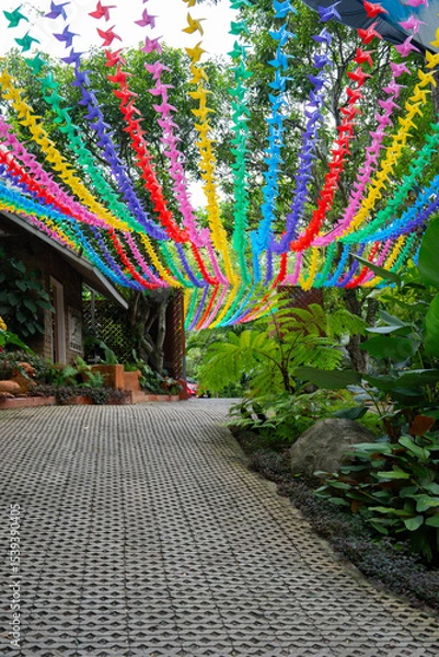 Obraz Colorful paper pinwheels hang above garden path, creating vibrant and festive atmosphere. path is lined with lush greenery