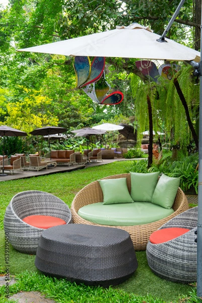 Obraz Outdoor seating area with wicker furniture and colorful cushions under umbrellas in lush garden setting