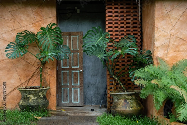 Obraz Rustic wooden door surrounded by lush green plants and terracotta walls creates serene entrance