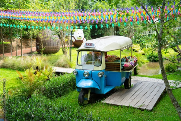 Obraz Colorful tuk tuk decorated with flowers sits in vibrant garden under canopy of multicolored ribbons