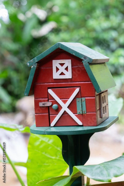 Obraz Small, red barn style mailbox with green roof stands in garden setting, surrounded by lush greenery