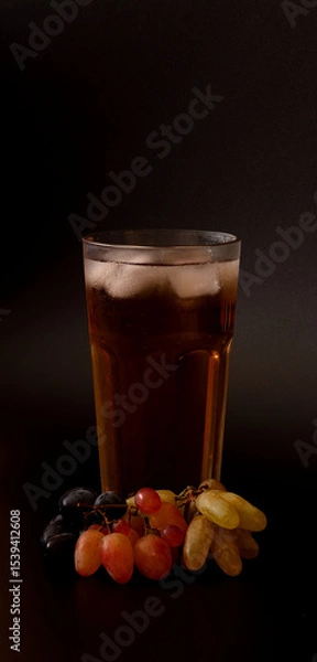 Obraz Tall glass of grape juice mixture with ice on black background, ripe bunches nearby.