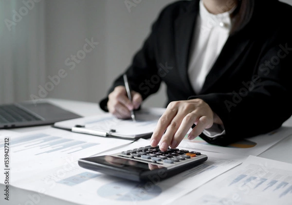 Fototapeta Young Asian business woman sitting at the table holding a pen, recording investments and planning the process of growing a successful business