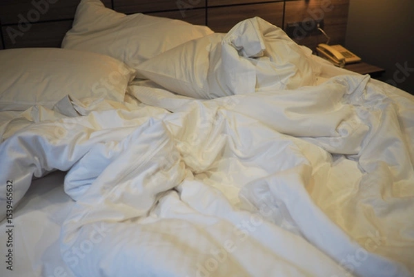 Fototapeta Messy bed with white sheets in a cozy hotel room