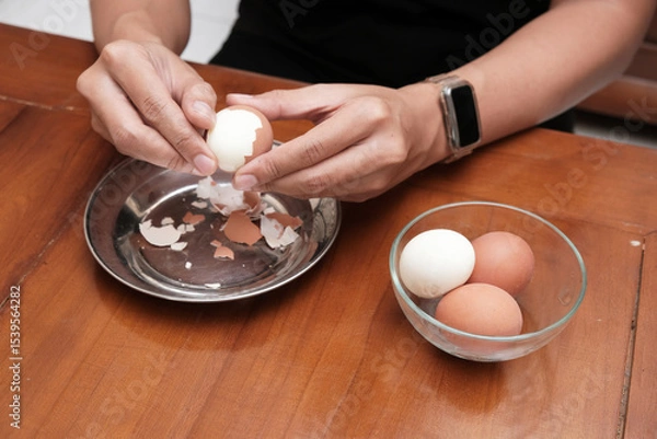 Obraz Close up of a man's hands peeling chicken boiled egg  on the kitchen table, prepares breakfast at home, health care and food concept. Copy space