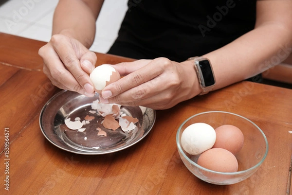 Obraz Close up of a man's hands peeling chicken boiled egg  on the kitchen table, prepares breakfast at home, health care and food concept. Copy space