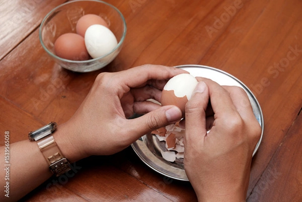 Obraz Close up of a man's hands peeling chicken boiled egg  on the kitchen table, prepares breakfast at home, health care and food concept. Copy space
