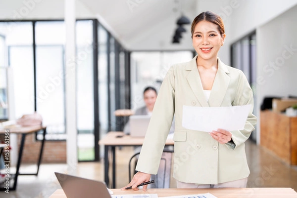 Obraz Female leader with a smile standing in the office and her team in the background. a woman boss and corporate business people at work