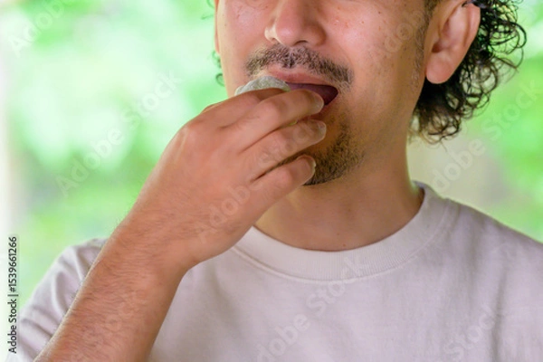 Obraz 和菓子をつまんだ男性がゆったりとした表情で口元に運ぶ夏の一瞬を切り取ったライフスタイル