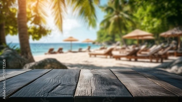 Fototapeta Empty dark wood table overlooking a sun-drenched, blurred tropical beach. An ideal paradise background for summer product displays, vacation mockups, travel promotions.