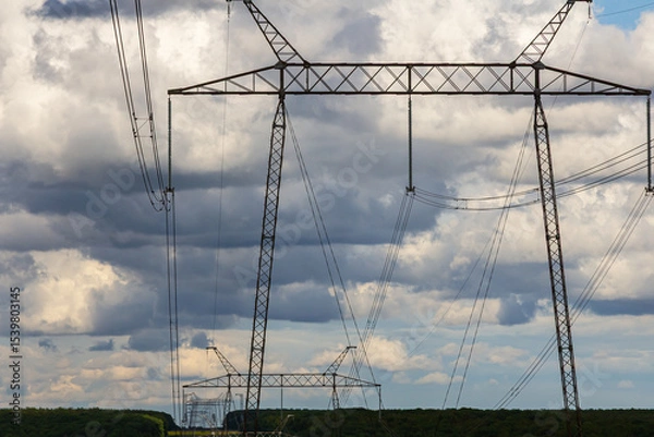Obraz High-voltage power lines stretch across a scenic landscape with dramatic clouds in the sky during late afternoon light