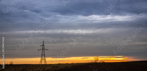 Obraz Sunset over a vast landscape with a lone power tower silhouetted against the colorful evening sky near a rural area