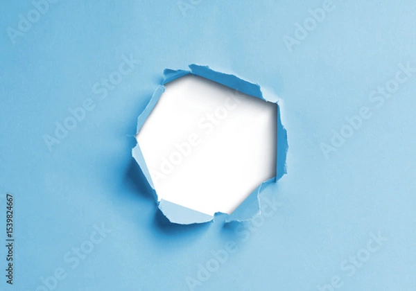 Fototapeta Close-up image of a blue paper sheet with a jagged hole torn through the center, revealing a transparent background.