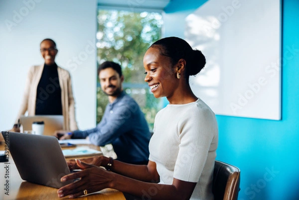 Fototapeta Businesspeople discussing in an office setting with focus on woman using laptop