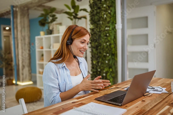 Obraz red head woman operator with headset talk on video call with client