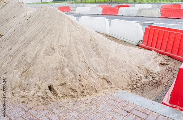 Fototapeta Pile of sand. Red and white plastic barriers blocking the road