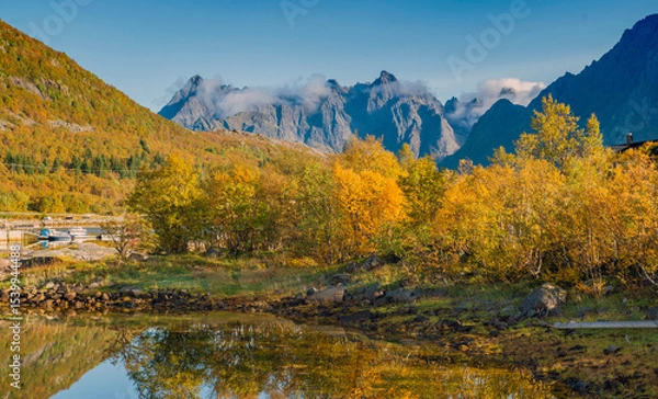 Fototapeta beautiful landscape of Norway with trees with yellow leaves reflecting in the water of a lake and mountain peaks in the background