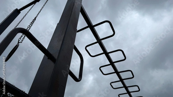 Obraz Metal monkey bars and gym rings on an outdoor playground against a dramatic cloudy sky – minimalist urban workout structure, low-angle view