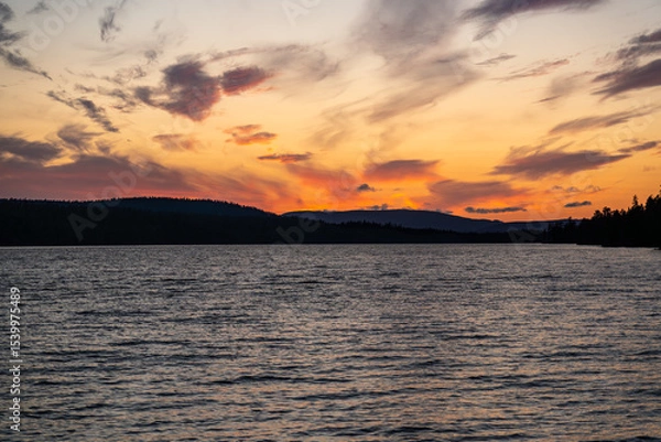 Fototapeta As the sun sets, vibrant colors reflect on Hällsjön lake, surrounded by the stunning Långfjället Nature Reserve in Sweden, offering a serene and picturesque view