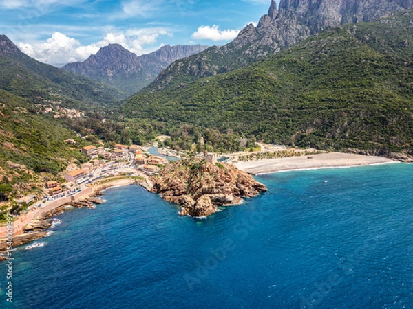 Fototapeta Aerial view of the Genoise tower on a rocky outcrop and the beach at Porto on the west coast of the Mediterranean island of Corsica with mountains behind