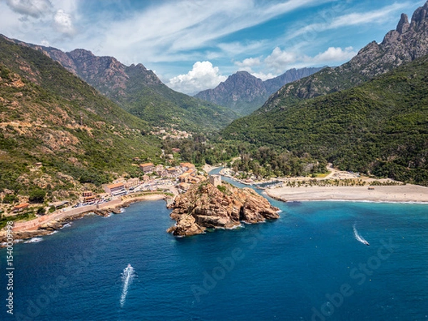 Fototapeta Aerial view of the Genoise tower on a rocky outcrop and the beach at Porto on the west coast of the Mediterranean island of Corsica with mountains behind