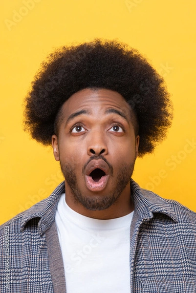 Fototapeta Surprised man looking up and reacts with shock on yellow background