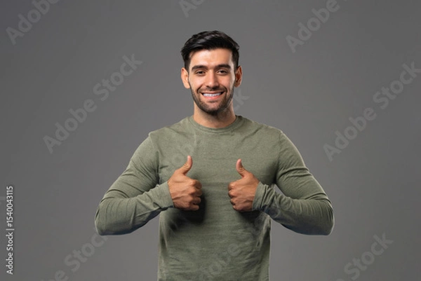Fototapeta Smiling handsome Caucasian man in casual long sleeve shirt showing double thumbs up on gray background