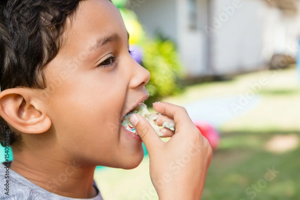 Obraz Biting into frosted cupcake with sprinkles while standing in front yard by white house, copy space