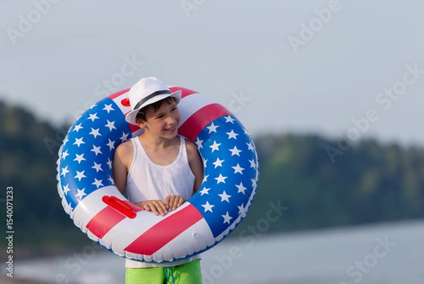 Obraz Child enjoying playing on beach with inflatable ring in american flag colors on sunny day