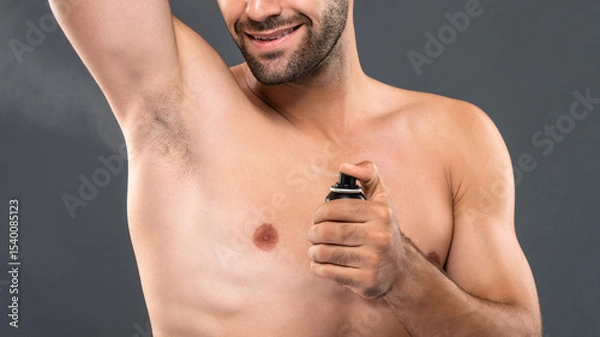 Fototapeta Closeup of young man spraying deodorant for body freshness and hygiene in gray studio banner background
