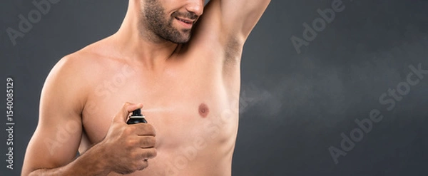 Fototapeta Closeup of young man spraying deodorant for body freshness and hygiene in gray studio banner background