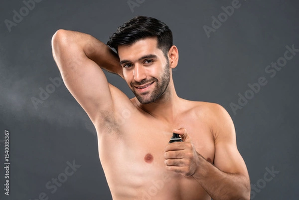 Fototapeta Handsome smiling young Caucasian man applying deodorant spray for hygiene and freshness