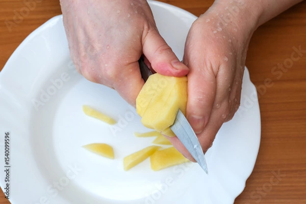 Obraz Hands skillfully peeling a fresh potato in a cozy kitchen setting