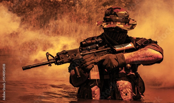 Obraz Soldier in camouflage, face covered, holding rifle in water with thick smoke behind.