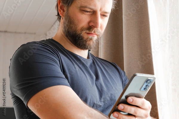 Fototapeta Man using his cellphone. Handsome guy use mobile phone at home. Male browses social networks, gaming, does shopping online, chats with friends, writes or reads messages. Close up. 4k video footage