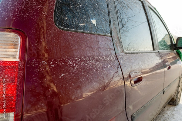 Fototapeta As the sun rose, the car was covered in a light blanket of snow. It was early morning. Frost appeared on the glass surfaces of the rear doors.