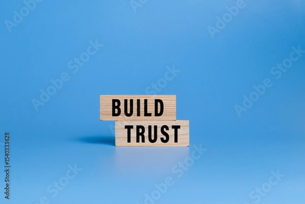 Fototapeta male hand putting wooden blocks with build trust words isolated on blue background
