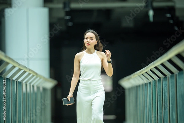 Fototapeta A woman is walking down a bridge with a cell phone in her hand