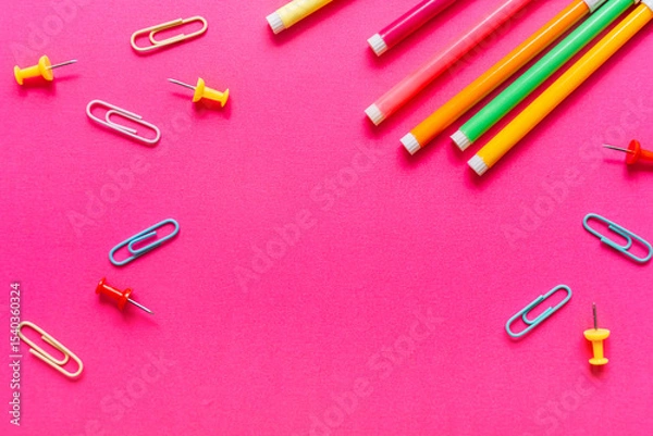 Fototapeta Brightly colored pens, paper clips, and push pins arranged on a vivid pink backdrop. Back to school concept in pop art style. High quality photo