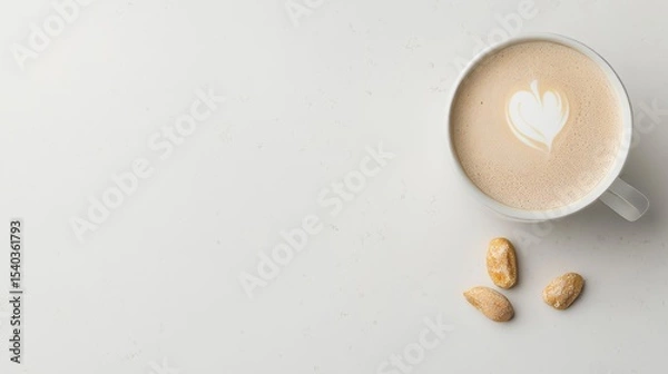 Fototapeta Minimalist top-down view of a cappuccino with heart-shaped latte art and scattered nuts on a clean white background. A calm, cozy setup perfect for cafe branding or morning coffee themes.