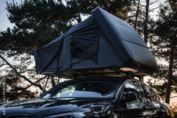 Obraz A modern SUV with a dark colored rooftop tent set up in a forest. Tall trees surround the vehicle as soft light filters through the branches.