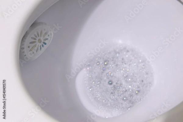 Obraz A toilet rim block creating foam in the water, set against a clean white background, symbolizing hygiene and freshness. Fresh and clean toilet rim