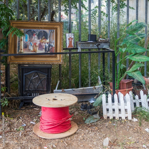 Fototapeta Petah Tikva, Israel, 12 June 2025, Miscellaneous Items and a Painting Against a Metal Fence. A place to relax in an abandoned area behind garages