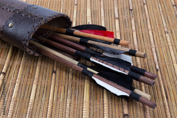 Fototapeta Different kinds of medieval handmade arrows with natural feathers in a handcrafted leather quiver on a bamboo rustic mat