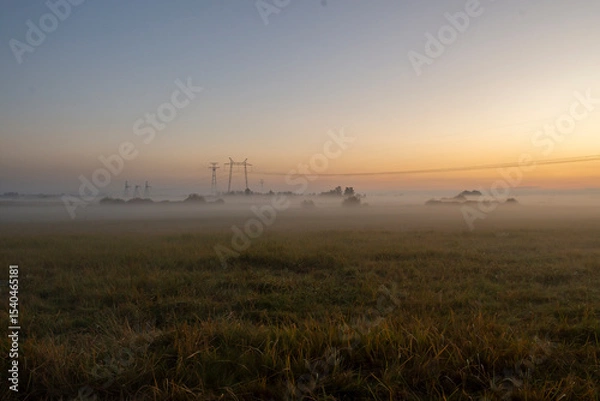 Fototapeta Dawn over a rural landscape with a tower of power lines and autumn fields