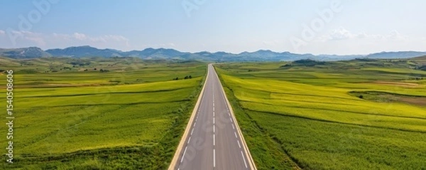 Fototapeta Construction infrastructure highway progress concept. Wide-open road stretching through lush green fields and distant mountains.