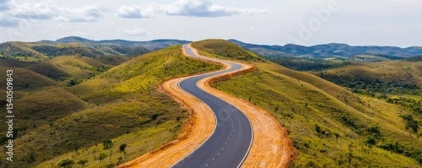 Fototapeta Construction infrastructure highway progress concept. Winding road through scenic hills under a cloudy sky.