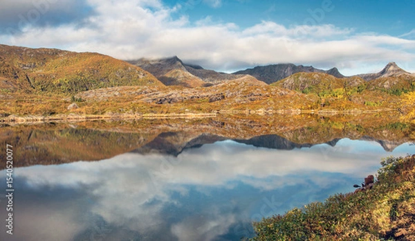 Fototapeta beautiful scenic autumnal landscape with mountaincovered with golden vegetation under the sky reflecting in surface of water in Norway.