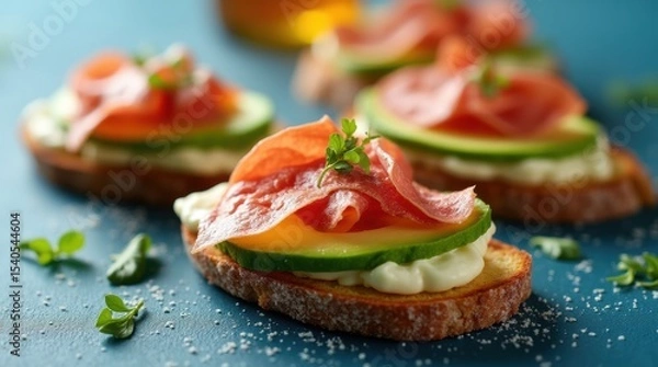 Obraz Mediterranean snacks with avocado, jamon, cheese on toasted bread, blue background, styled for food photography and menu.