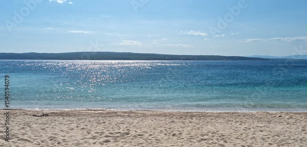 Obraz A view from the sandy Poli Mora beach in Selce, with shimmering turquoise sea in the foreground and Krk Island in the distance under a sunny sky